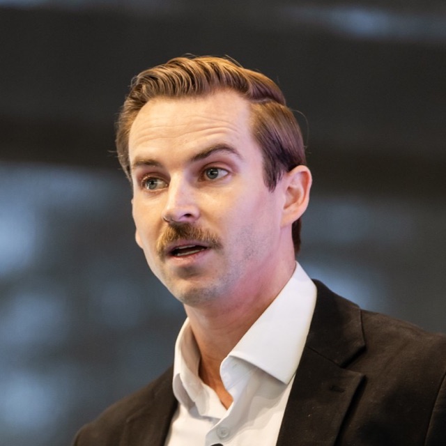 Lucas Miller speaking, in a dark blazer and white shirt